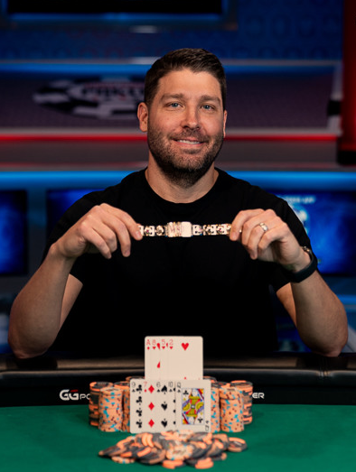 Jeremy Ausmus holding a WSOP gold bracelet at the poker table with his winning hand and chips